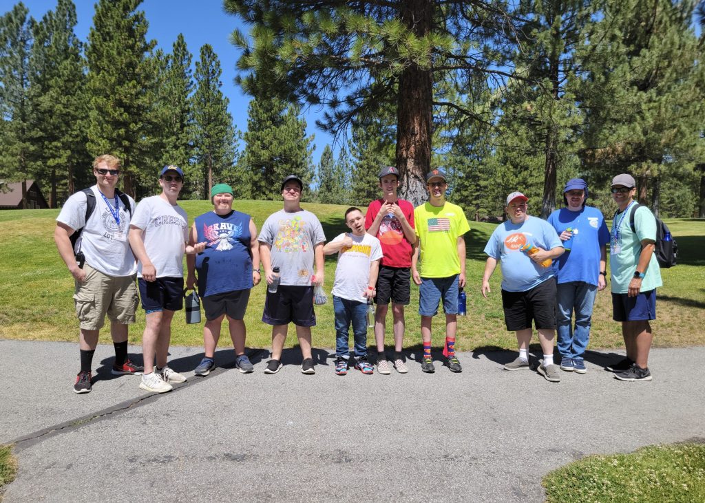 Group of Amplify Life campers smiling under tall pine trees