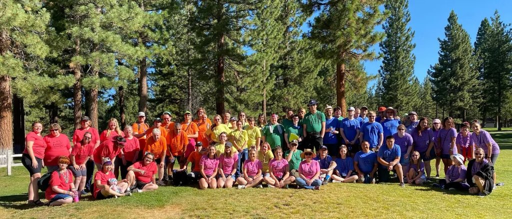 Amplify Life community gathered in colorful shirts under tall pine trees